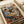 May include: Vintage-style poster print featuring two anthropomorphic cats in a cozy café setting. One tabby cat wears a black beret and striped shirt, sitting across from an orange cat in a floral dress. They share coffee and pastries at a small round table with an espresso machine in the background. Cat portraits hang on cream walls. The artwork has warm, muted tones and appears mounted on cream paper against a beige surface.