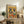 May include: Framed poster artwork displayed on rustic wooden credenza featuring two French bulldogs in colorful Mexican attire enjoying a feast with tacos, guacamole, and tequila bottles on vibrant yellow and orange background. Room scene shows neutral walls, fern plant, ceramic vase, books, and beige upholstered furniture creating cozy home decor setting.