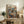 May include: Framed poster print displayed on rustic wooden sideboard showing two anthropomorphic cats sitting at cafe table with coffee cups and pastry, coffee machine in background, colorful illustrated art style with "CAT CAFÉ" text at top, surrounded by books, ceramic vase, and fern plant in cozy living room setting