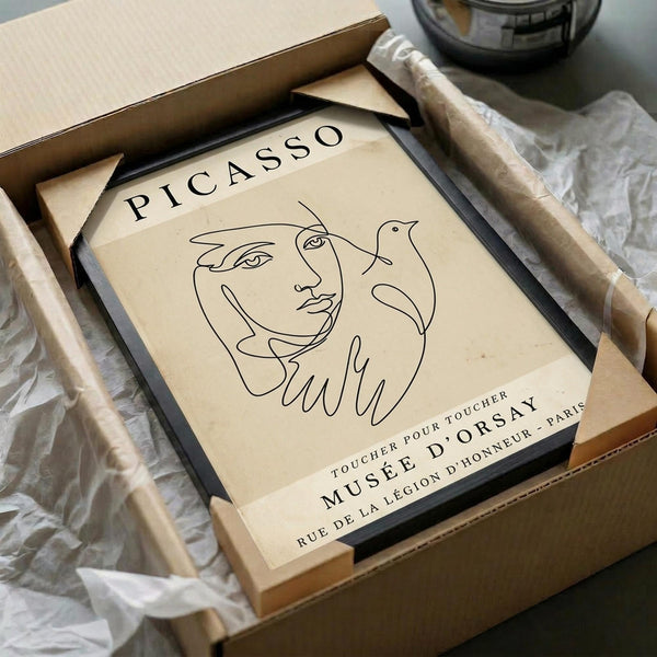 May include: Minimalist line art poster featuring abstract face and dove design in black on cream background, displayed in black frame within cardboard packaging with tissue paper, surrounded by wooden craft sticks on white surface