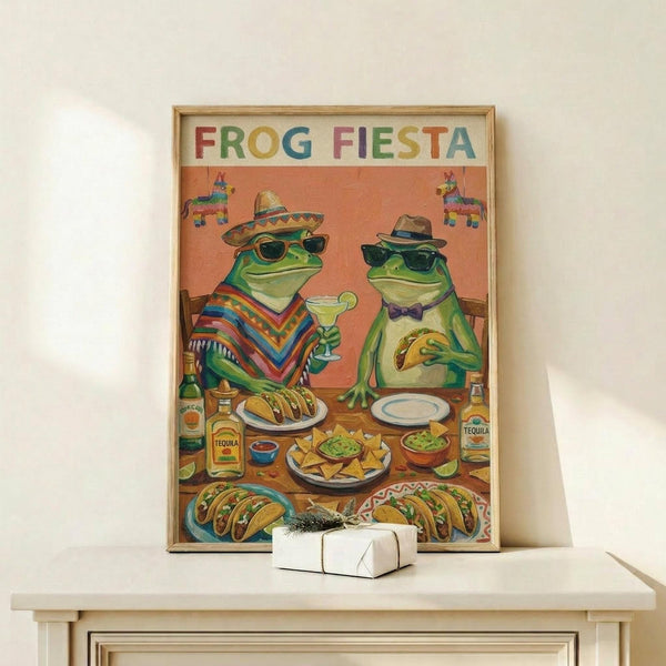 May include: Framed poster displaying two cartoon frogs wearing sunglasses and Mexican hats sitting at a table with tacos, margaritas, and tequila bottles. The artwork features bright colors with "FROG FIESTA" text at top and piñatas in background. Natural wood frame sits on white wooden surface next to small wrapped gift box against cream wall.