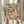 May include: Hands holding a framed print featuring a colorful mosaic pattern of vintage book spines in various sizes, colors including blues, oranges, creams, and reds. Person wears beige clothing with ruffled sleeves, holding dried wheat stems. Soft natural lighting against neutral curtained background creates cozy reading nook atmosphere.