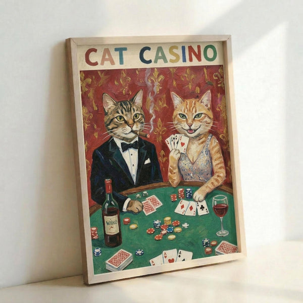 May include: Framed vintage-style poster showing two anthropomorphic cats in formal attire at a green poker table. The tabby cat wears a black tuxedo with bow tie, while the orange cat wears a sparkly dress and holds playing cards. Red ornate wallpaper background, casino chips, wine bottle and glass, scattered playing cards on felt table. Light wooden frame leaning against white wall.