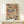 May include: Framed poster print featuring a colorful mosaic pattern of vintage book spines in various sizes, arranged in a Tetris-like composition. Books display muted tones of blue, orange, red, cream, and green with visible text details. Natural wood frame displayed on light wooden surface alongside white wrapped gift with evergreen sprig. Clean white wall background with soft natural lighting creates minimalist styling.