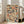 May include: Framed poster print leaning against white wall next to beige sofa in bright living room with large windows. Artwork shows colorful mosaic pattern of stacked book spines in various sizes and colors including red, blue, orange, cream, and green tones arranged in geometric blocks. Light wood frame, hardwood floors visible.