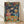 May include: Framed poster print leaning against white wall on light wooden floor. Colorful retro-style artwork shows cat in pink spacesuit and dog in blue NASA suit with helmets, toasting champagne glasses in space. Galaxy background with planets and stars. Table spread includes fried chicken bucket, plates of food, french fries, and dark soda bottles labeled Space Cola. Vibrant rainbow lettering at top. Natural lighting creates soft shadows on textured white fabric backdrop.