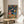 May include: Framed poster featuring a cat astronaut in pink spacesuit and dog astronaut in blue spacesuit toasting with glasses in space. They sit at a table with fried chicken, fries, and drinks against a starry galaxy background with colorful planets. The vintage-style artwork is displayed on a round wooden side table next to a beige upholstered chair in a bright, minimalist room with white walls and natural lighting.