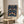 May include: Framed poster with William Morris's iconic Strawberry Thief pattern featuring symmetrical birds, strawberries, and flowers in deep blue, green, coral and cream colors. The vintage-style botanical design sits in a natural wood frame on a round wooden side table next to a beige upholstered chair, with soft natural lighting and a plant visible in the background.
