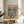 May include: Framed poster print displayed on a round wooden side table next to a beige upholstered chair. The artwork features two cartoon ducks on a yacht deck at sunset - one wearing a floral shirt and sun hat, the other in a striped nautical shirt and captain's hat. They're toasting with champagne glasses while enjoying a spread of gourmet food including lobster, caviar, and cheese. The colorful illustration shows other boats in the background on blue water with an orange sunset sky.