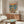 May include: Whimsical poster artwork showing two cartoon ducks in summer outfits toasting champagne on a yacht deck at sunset, with boats visible on blue water in background. The colorful illustration is displayed in a thin wood frame above a mid-century modern walnut credenza with white ceramic table lamp. A cream upholstered swivel chair and oval glass coffee table with wood base complete this bright, contemporary living room setting with white walls.