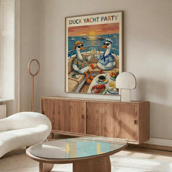 May include: Whimsical poster artwork showing two cartoon ducks in summer outfits toasting champagne on a yacht deck at sunset, with boats visible on blue water in background. The colorful illustration is displayed in a thin wood frame above a mid-century modern walnut credenza with white ceramic table lamp. A cream upholstered swivel chair and oval glass coffee table with wood base complete this bright, contemporary living room setting with white walls.