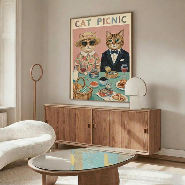 May include: Whimsical illustrated poster showing two dressed cats at a picnic table with gourmet foods, displayed above a mid-century modern walnut credenza in a bright living room with white curved chair, glass coffee table, and warm natural lighting creating soft shadows on neutral walls.