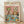 May include: Framed poster print leaning against white wall on light wooden floor. Artwork shows two anthropomorphic cats at spa day - one wearing green cucumber eye mask holding wine glass, another with face mask and hair towel. Table displays spa items, fruit plates, cheese, and wine bottle labeled "Purrfection." Colorful text reads "CAT SPA DAY PAWS & RELAX" at top. Natural wood frame, vintage illustration style with warm pink and teal colors.