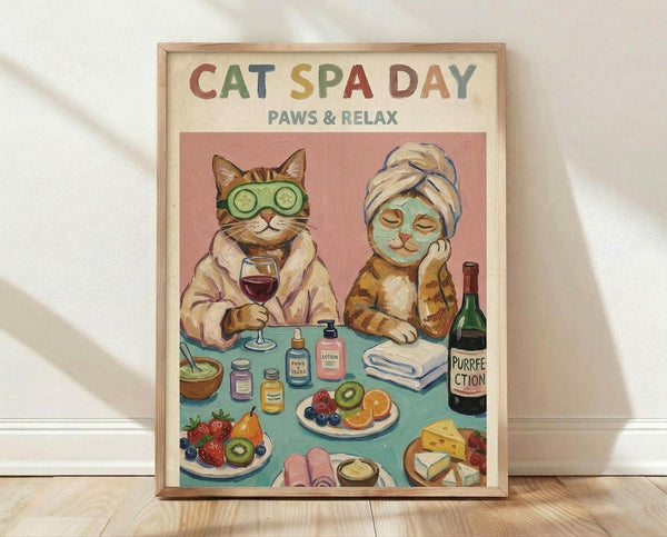 May include: Framed poster print leaning against white wall on light wooden floor. Artwork shows two anthropomorphic cats at spa day - one wearing green cucumber eye mask holding wine glass, another with face mask and hair towel. Table displays spa items, fruit plates, cheese, and wine bottle labeled "Purrfection." Colorful text reads "CAT SPA DAY PAWS & RELAX" at top. Natural wood frame, vintage illustration style with warm pink and teal colors.