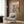 May include: Framed poster showing two illustrated cats at a spa table with face masks, cucumber eye patches, wine, and spa items on pink and teal background. Displayed above a beige upholstered chair with geometric pillow in modern room with wood paneling, floor lamp, and side table.
