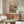 May include: Framed poster showing two cartoon cats in pajamas napping on a pink armchair, with colorful "CAT NAP" text at top. Displayed above a wooden mid-century credenza in a bright living room with white curved chair, glass coffee table, and modern lamp. Warm wood tones throughout the minimalist space with cream walls and natural lighting.