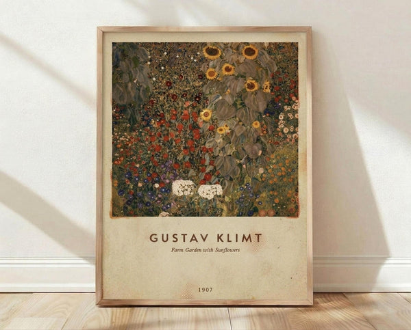 May include: Framed art print leaning against white wall on light wood floor. The poster features Gustav Klimt's colorful floral painting with sunflowers, red poppies, and wildflowers in decorative pattern style. Natural wood frame with cream matting. Soft window light creates gentle shadows on textured wall. Print shows artist name and 1907 date below the artwork.