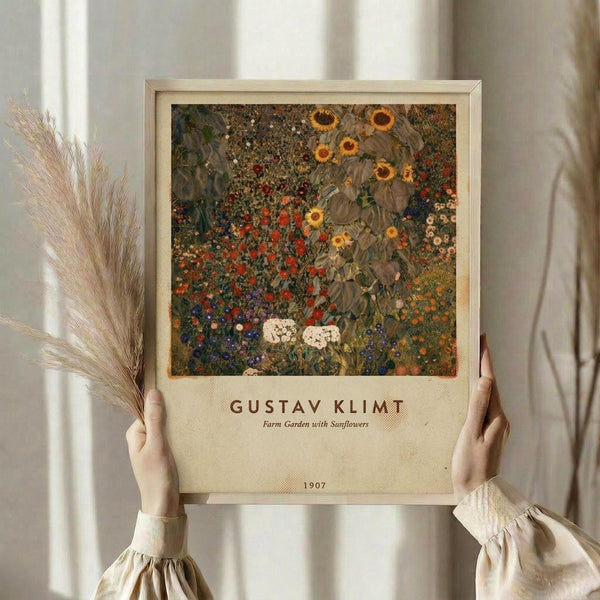 May include: Person in cream ruffled sleeves holding framed art print against white curtained window, with dried wheat stalks nearby. The vintage-style poster features Gustav Klimt's colorful garden painting with sunflowers, red poppies, and wildflowers in rich greens, golds, and earth tones, displayed in light wood frame with cream matting.