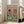May include: Framed poster print leaning against white wall next to beige sofa in bright living room. Artwork shows anthropomorphic tabby cat in striped shirt and beret alongside shaggy dog in floral Hawaiian shirt, both wearing sunglasses at brunch table with croissants, wine, cheese board, and bread. Pink and teal color scheme with colorful title text at top.