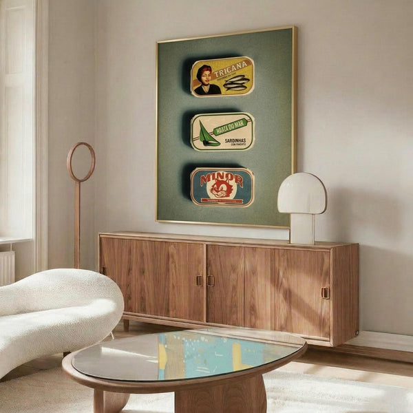 May include: Three vintage Portuguese sardine can labels displayed in a framed green artwork above a mid-century walnut credenza. The labels show "Tricana," "Prata Do Mar," and "Minor" brands with colorful retro designs. Scene includes a white curved chair, brass floor lamp, modern mushroom table lamp, oval glass coffee table, and cream textured rug in a minimalist living room with white walls.