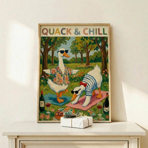 May include: Framed poster with colorful illustration of two ducks in sunglasses relaxing outdoors - one wearing a floral shirt standing by water, another in striped shirt doing yoga on a pink mat. Scene shows green trees, wine bottles, and "QUACK & CHILL" text at top. Light wood frame sits on white wooden console table with small wrapped gift beside it against cream wall.