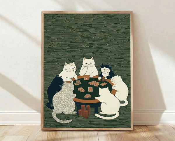 May include: Framed print showing five cats sitting around a dark green poker table playing cards in Japanese woodblock art style. Cats are white, black, and striped, positioned around wooden table with playing cards and poker chips. Green textured background with horizontal line pattern. Natural wood frame displayed on light wooden floor against white wall with soft shadows.