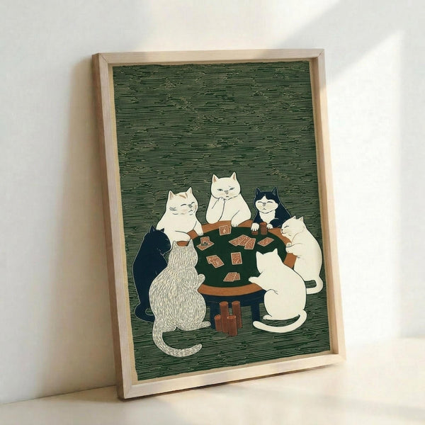 May include: A framed print leaning against a white wall showing six cats of various colors sitting around a green poker table playing cards. The artwork features a traditional Japanese woodblock print style with fine line work and muted colors against a sage green textured background. The light wooden frame complements the earthy tones of the illustration.