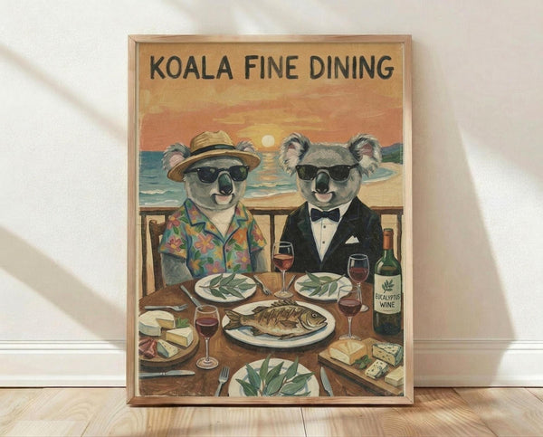 May include: Framed vintage-style poster print leaning against white wall on light wood floor. Features two koalas in sunglasses dining at seaside restaurant - one in tropical shirt and hat, other in black tuxedo. Eucalyptus wine bottle, fish dinner, cheese board visible on wooden table with ocean sunset backdrop. Warm orange and teal color palette in weathered illustration style.