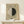 May include: Framed museum exhibition poster featuring Hilma af Klint's abstract geometric artwork - a circle split into white and black halves with thin horizontal lines, displayed on light wooden shelf with small wrapped gift box beside it against cream wall