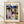 May include: A framed poster displaying Paul Klee's abstract geometric artwork with colorful triangular roofs, rectangular buildings, and shapes in blues, yellows, greens, and earth tones. The cream-colored print features "KLEE" at the top and "BAUHAUS ARCHIV JUBILÄUM 1919-2019" at the bottom. The natural wood frame leans against a white wall on light wooden flooring with soft shadows visible.