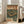 May include: Vintage-style Japanese poster in light wood frame leaning against white wall next to beige couch. Green and orange retro design features turntable with vinyl record and cassette player with headphones. Japanese text in bold orange letters at top. Warm sunlight streams through windows onto hardwood floor in modern living room setting.