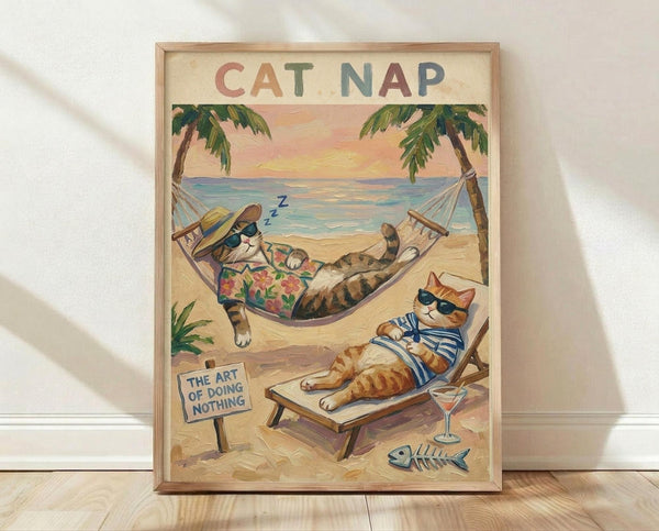 May include: Framed poster print leaning against white wall on light wood floor. Artwork shows two cats relaxing on tropical beach - one tabby in Hawaiian shirt sleeping in hammock between palm trees with "Z" sleep symbols, another orange tabby in striped shirt lounging on beach chair wearing sunglasses. Beach scene includes martini glass, fish skeleton, small sign reading "THE ART OF DOING NOTHING." Sunset sky with pink and orange hues over ocean. Vintage illustration style in warm tone