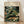 May include: Framed poster print featuring Henri Rousseau's jungle artwork with a resting tiger among lush tropical foliage in deep greens, yellows, and coral tones. White flowers and palm fronds surround the spotted big cat. The cream-colored poster displays "HENRI ROUSSEAU" and "NATIONAL GALLERY OF MODERN ART" text at top. Light wood frame sits against white wall on wooden floor with natural lighting casting soft shadows.