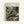 May include: Framed art print featuring Henri Rousseau's jungle scene with a spotted leopard resting among lush tropical foliage. Dense green palm fronds and leaves fill the composition with delicate white and pink flowers scattered throughout. The poster has cream-colored text at the top reading "Henri Rousseau" and "National Gallery of Modern Art" with exhibition details. Natural wood frame against white wall background.