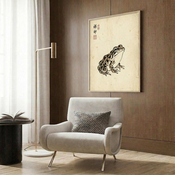 May include: Japanese-style frog artwork displayed in modern living room with beige armchair, geometric pillow, brass floor lamp, and dark wood paneling. The vintage-inspired print features a spotted frog on aged paper with Asian calligraphy, framed and hung above a minimalist seating area with warm neutral tones throughout.