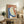 May include: Abstract artwork in light wood frame displayed on rustic wooden sideboard beside fern plant, books, and ceramic vases. Artwork features organic oval shapes in terracotta orange, sage green, and deep blue with textured brushstrokes and small cream circle, set against neutral living room with beige chair and warm lighting.