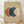 May include: Framed abstract art print featuring three overlapping circles in terracotta orange, deep blue, and cream colors on textured beige background. Displayed in light wood frame leaning against white textured wall above light wooden flooring with natural shadows cast across the scene.