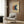 May include: Abstract art print featuring three overlapping circles in orange, navy blue, and cream colors on beige background, displayed above modern beige armchair with geometric patterned pillow. Room setting shows wood paneled wall, brass floor lamp, and dark round side table with open book.