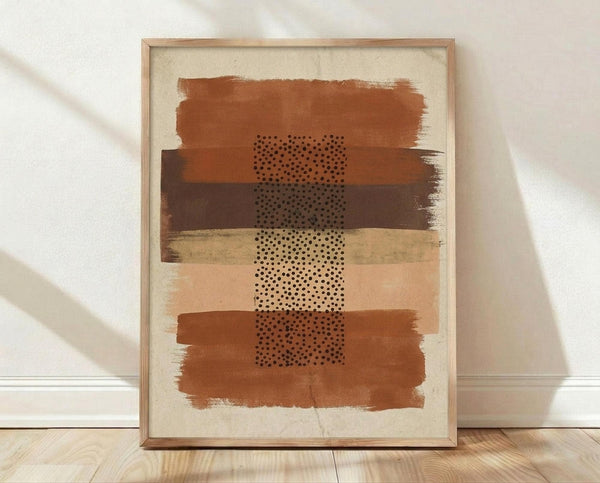 May include: Framed abstract art print leaning against white textured wall on light wood floor. Artwork features horizontal brushstrokes in terracotta, ochre, and brown tones with vertical column of black polka dots down center. Natural wood frame with warm earth-toned palette on cream background. Soft natural lighting creates diagonal shadows across wall.