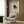 May include: Kandinsky abstract geometric art poster in light wood frame hanging on wood paneled wall above cream upholstered armchair with geometric pillow. Floor lamp with brass finish stands nearby next to dark round side table with open book. Poster features colorful triangles, circles and lines in red, blue, yellow, green and black on cream background.