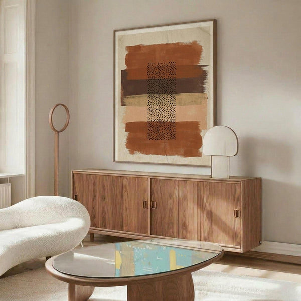 May include: Abstract art print in wooden frame hanging above mid-century walnut sideboard in neutral living room. Artwork features horizontal brushstrokes in terracotta, brown, and cream tones with black dotted pattern down center. Modern curved white chair and glass-top coffee table visible. Natural lighting creates warm shadows on beige walls.