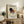 May include: Framed Kandinsky exhibition poster with abstract geometric shapes in black, burgundy, yellow and blue displayed on rustic wooden sideboard next to fern plant, books, and ceramic vases in neutral-toned living room setting