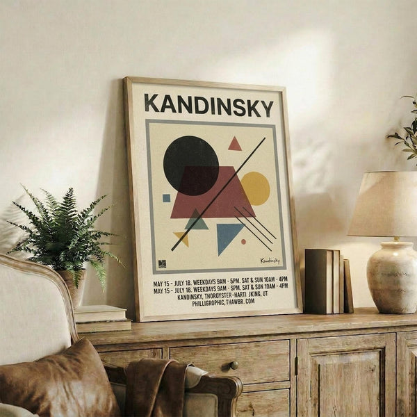 May include: Framed Kandinsky exhibition poster with abstract geometric shapes in black, burgundy, yellow and blue displayed on rustic wooden sideboard next to fern plant, books, and ceramic vases in neutral-toned living room setting