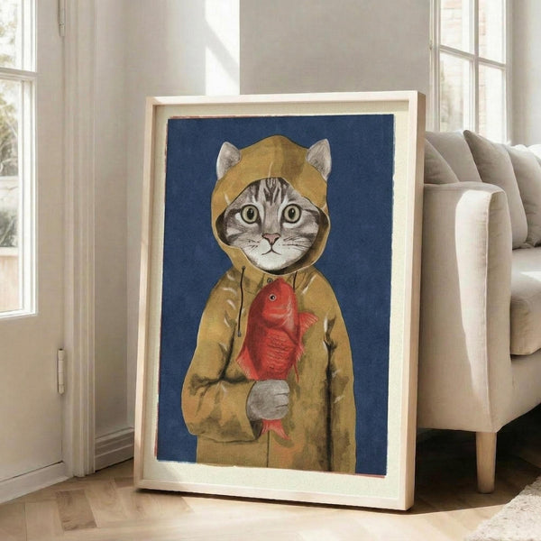 May include: Framed artwork showing a tabby cat wearing a yellow hooded raincoat and holding a red fish, set against a deep blue background. The illustration has a whimsical, painterly style with soft textures. The light wood frame leans against a white wall next to a beige upholstered chair in a bright, modern living room with large windows and natural lighting.