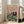 May include: Framed vintage-style poster showing two elegantly dressed ducks at a formal dinner table. The female duck wears a sparkly dress with fur stole, the male duck sports a burgundy tuxedo with bow tie and monocle. They're dining at a green tablecloth-covered table with multiple plates of food, champagne glasses, and candles. The poster has "FANCY DUCKS" text at top in colorful letters against a pink background. Frame leans against white wall near beige couch in bright room.