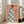 May include: Framed art print leaning against white wall next to beige sofa showing woman from behind wearing blue robe with white magnolia flower pattern, small bird perched on her shoulder, coral pink background, natural lighting from windows, light wood frame on hardwood floor