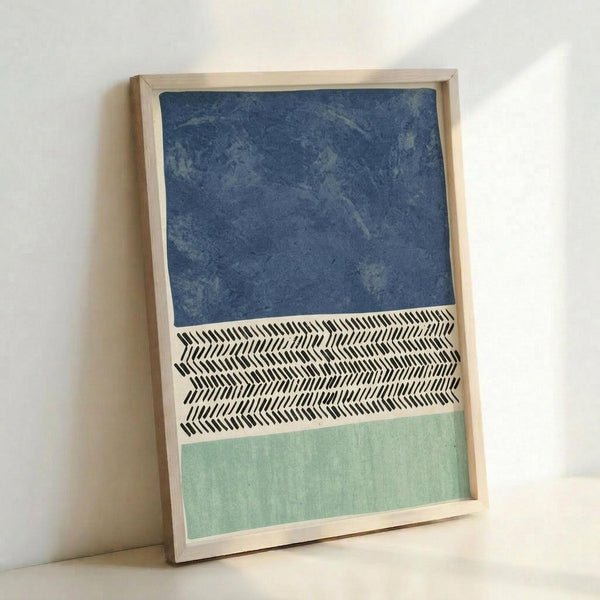 Framed abstract artwork with three horizontal sections: textured navy blue at top, black and white herringbone chevron pattern in middle, and soft sage green at bottom. The piece is displayed in a light wood frame, leaning against a white wall on a light surface.