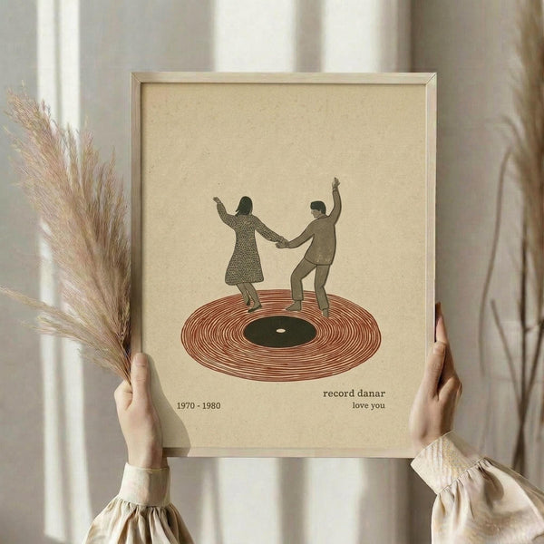 May include: Hands holding a framed vintage-style poster showing two people dancing on a vinyl record. The artwork features earth tones with a cream background, reddish-brown record, and silhouetted figures in 1970s clothing. Text reads "record danar 1970-1980 love you" below the illustration. Natural lighting illuminates the scene with dried pampas grass visible to the left.