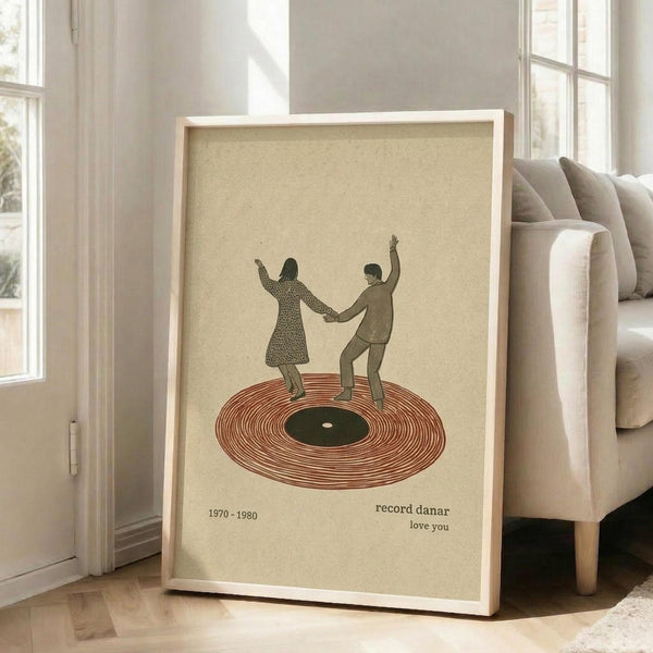 May include: Framed vintage-style poster leaning against beige sofa in bright living room with hardwood floors and white walls. The artwork features two people dancing on a large vinyl record with "1970-1980" and "record danar love you" text on cream background. Natural lighting streams through tall windows.