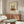 May include: Vintage-style poster print in thin brown frame hanging above wooden mid-century credenza. Artwork shows two silhouetted figures dancing on red vinyl record with cream background and text reading "record danar love you 1970-1980". Room features white curved chair, oval glass coffee table, modern white lamp, and neutral walls with natural lighting.